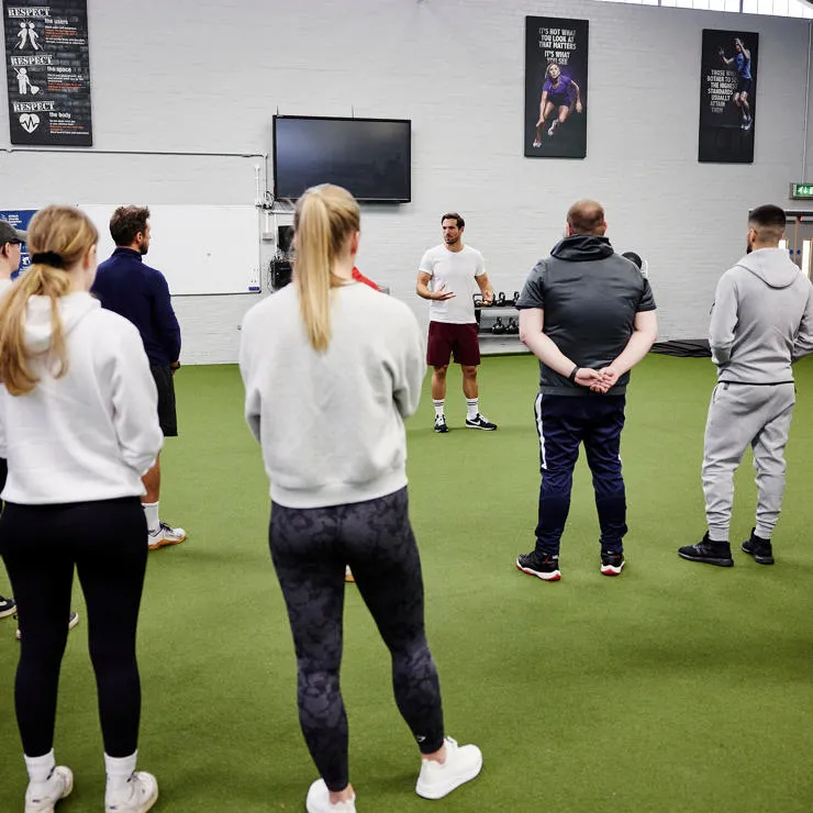 Students stood listening to a lecturer in the PEC.