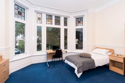 A Waldegrave Park House room with large window, a single bed, a desk, and blue carpet.