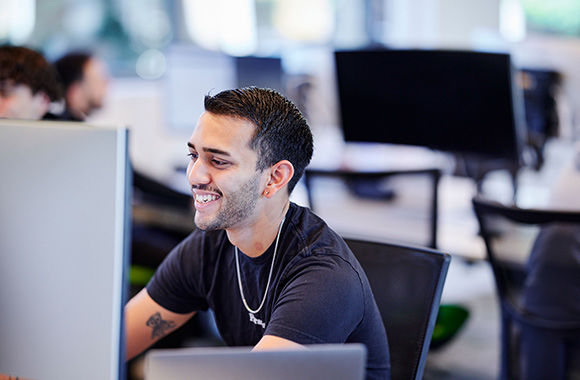 A student sits by a computer in a computing lab.