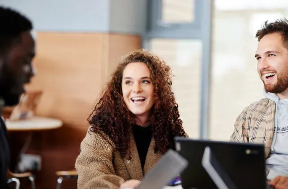 Students laughing while sat around a table.