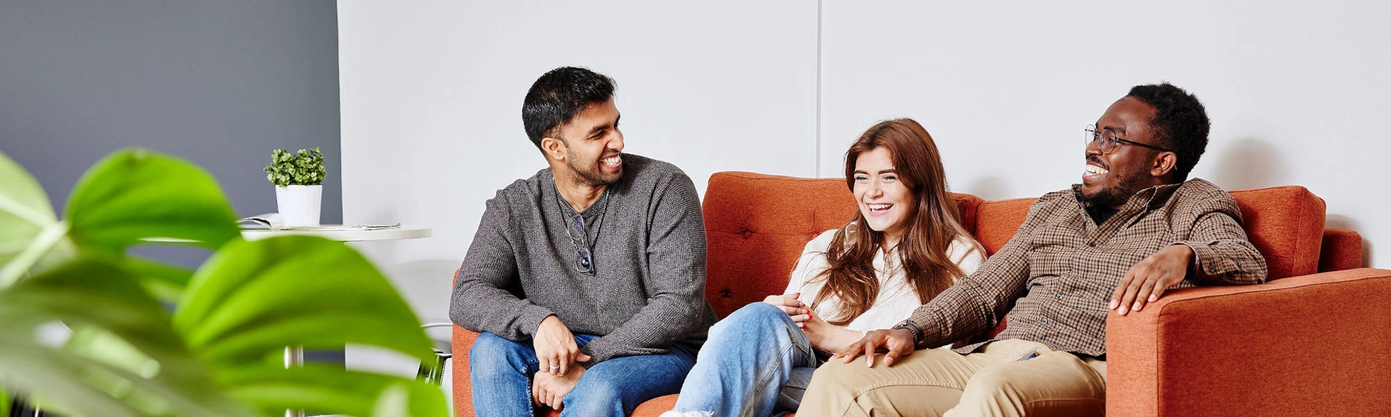 Three students sit on a sofa talking to one another.