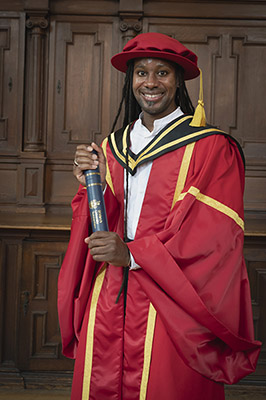 Prof Jason Arday in acaemic robes holding degree in academic tube